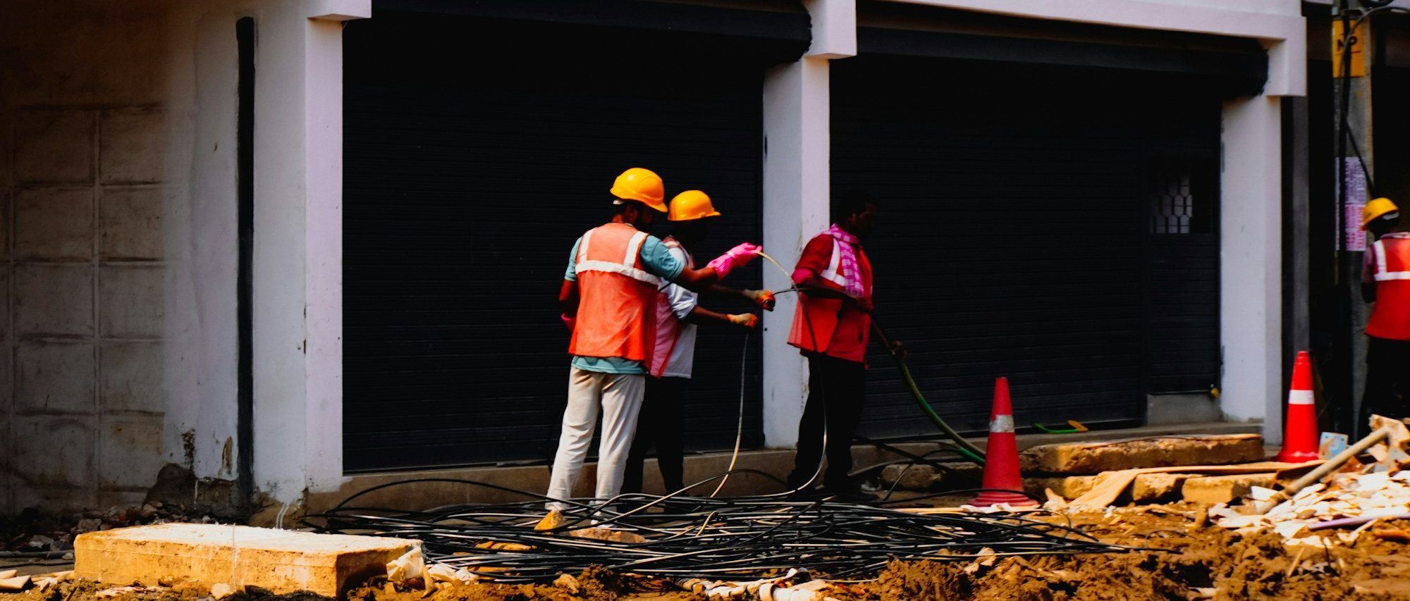 Trabajadores con casco y chaleco reflectante en el acceso de una obra, frente a las cortinas metálicas del edificio en construcción.