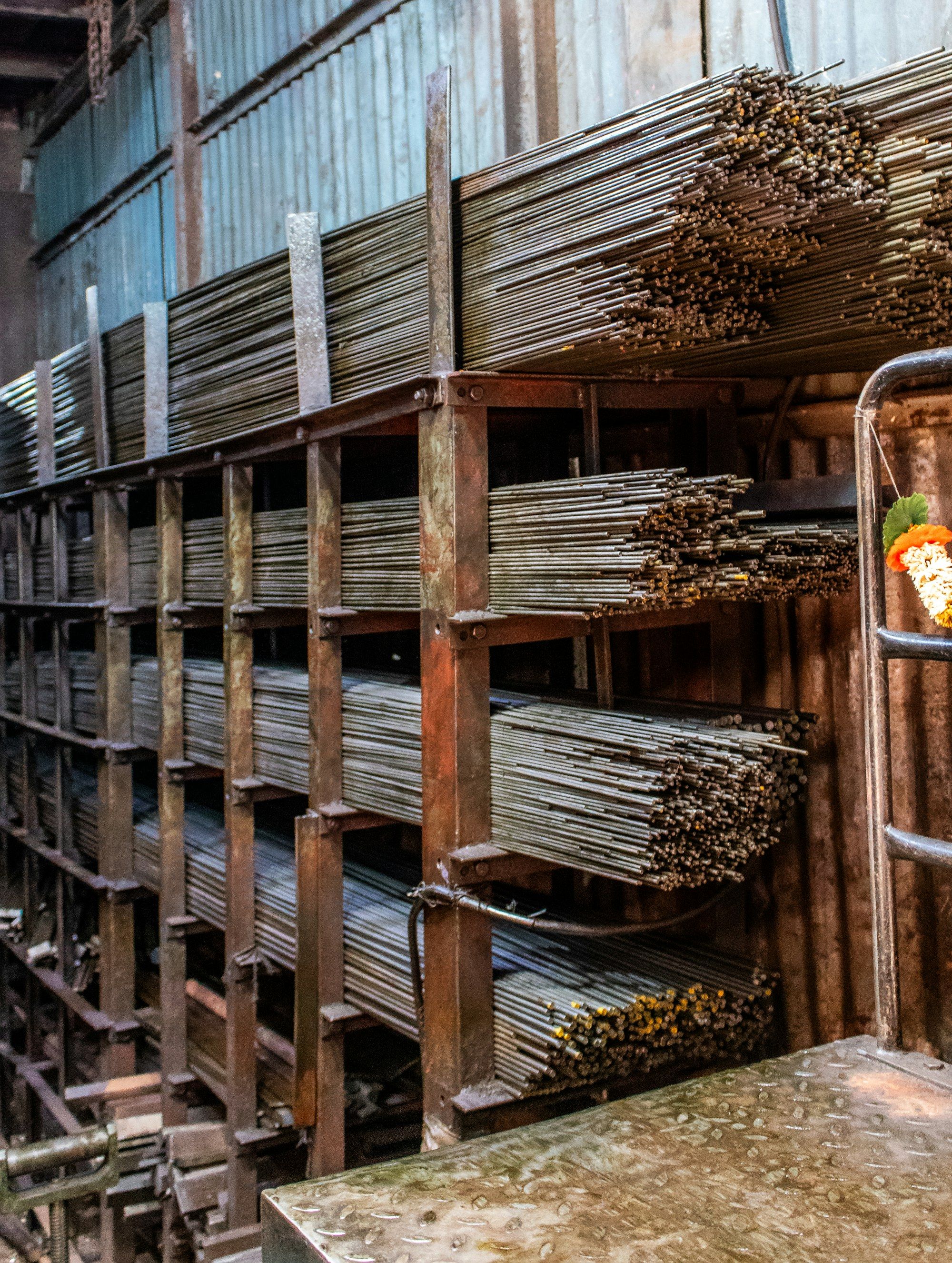 Estanterías de acero en una bodega, cargadas con paquetes de barras de fierro ordenados por diámetro en cada nivel.