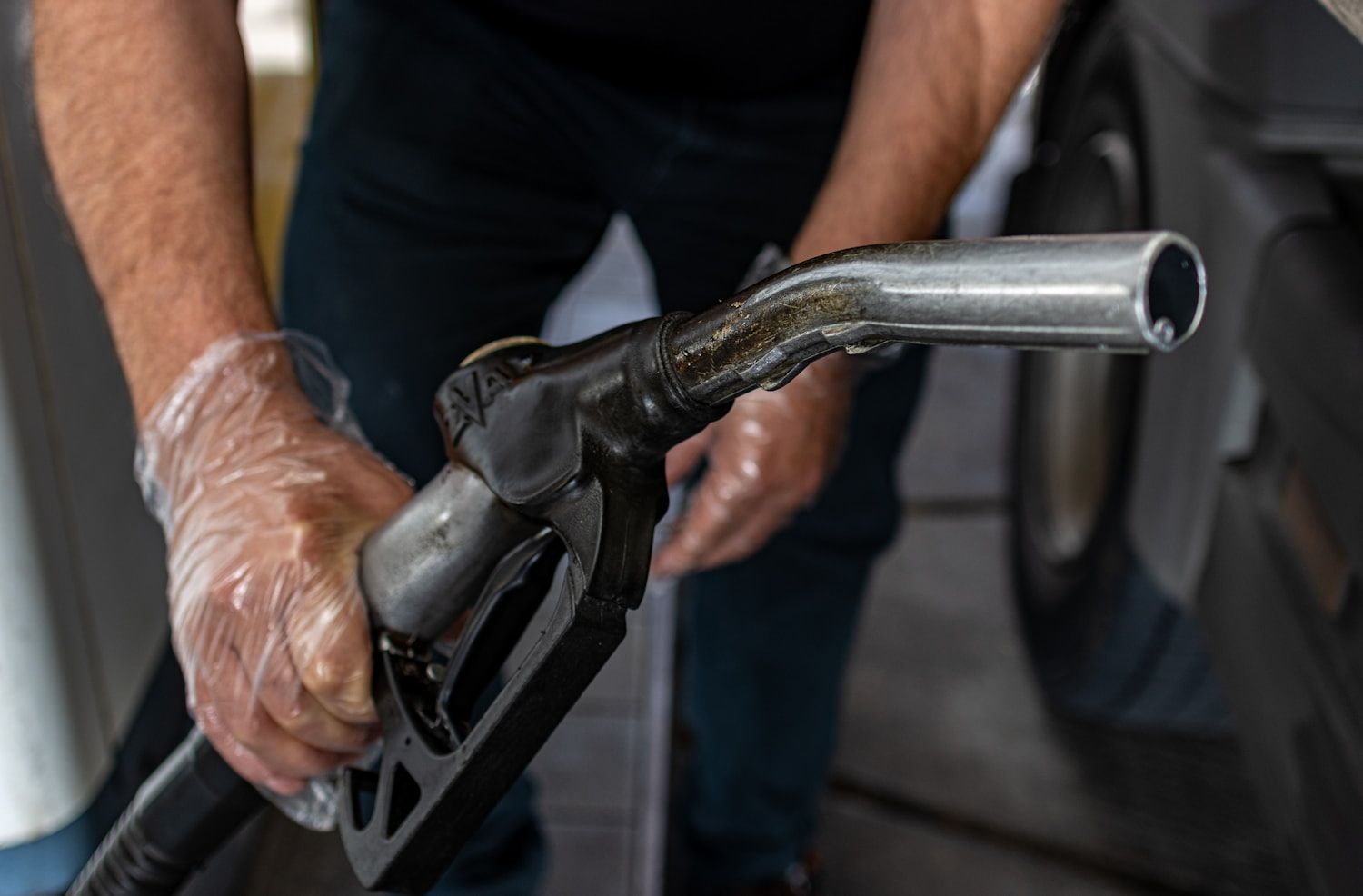 Manos sosteniendo la pistola de un surtidor de combustible, con la boquilla metálica hacia adelante.