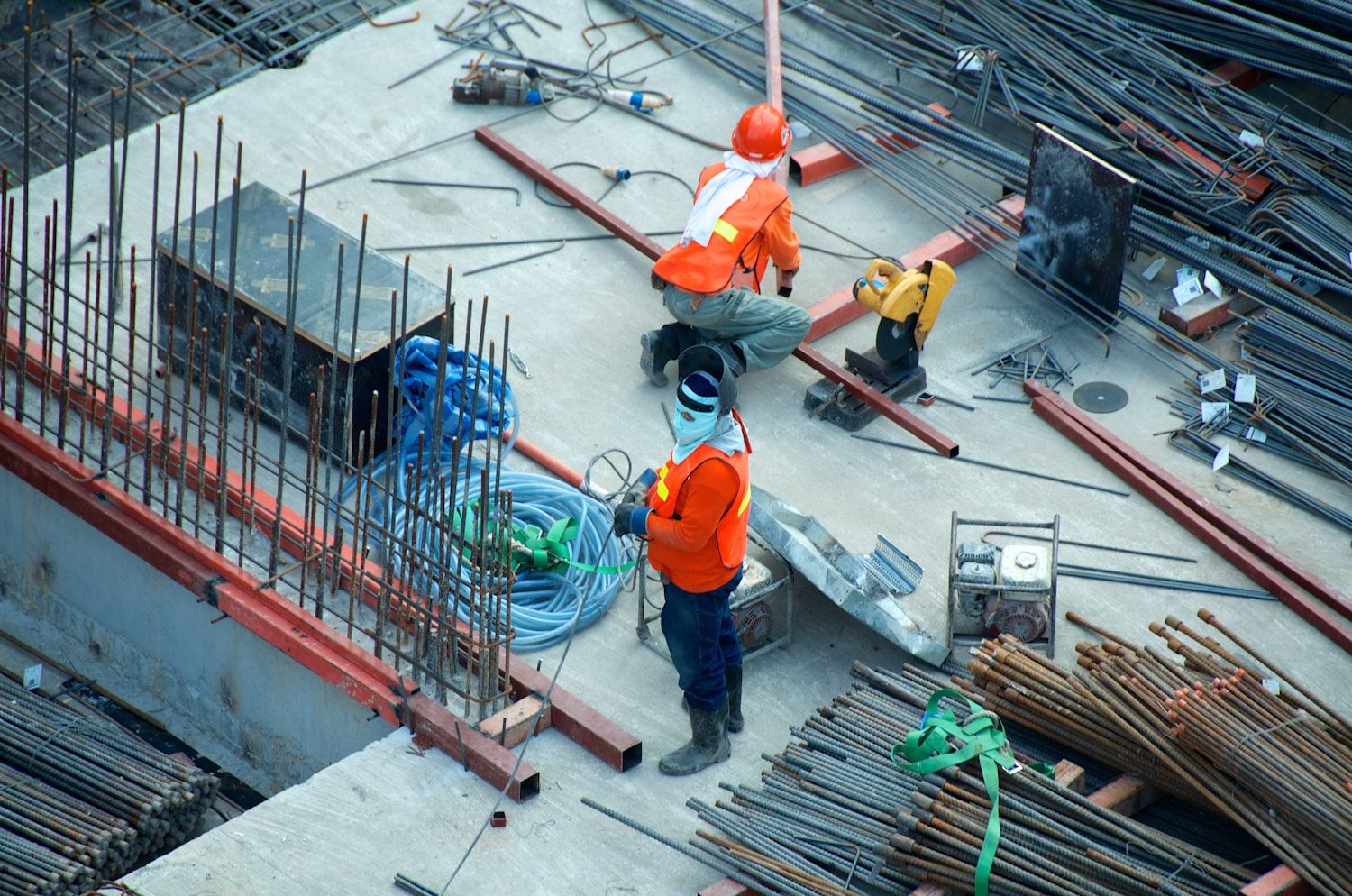 Vista desde arriba de dos trabajadores con casco y chaleco reflectante sobre una losa en construcción, entre enfierradura y rollos de manguera.