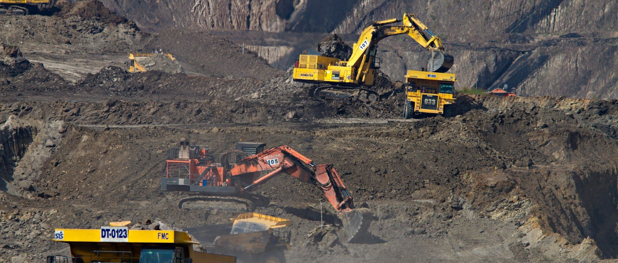 Faena a rajo abierto vista desde lejos: excavadoras y camiones de alto tonelaje trabajando en distintos niveles del banco.